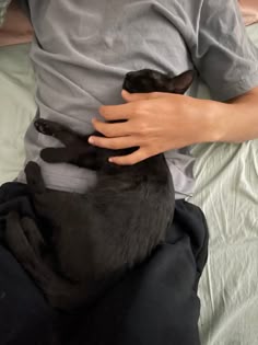 a person laying in bed holding a black cat