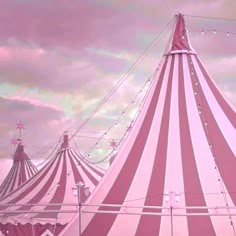 a pink and white striped circus tent with string lights on the top in front of a cloudy sky