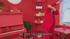 a woman in a red dress standing next to a pink room with shelves on the wall