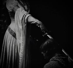 a black and white photo of a woman in a dress holding a knife to another person's head