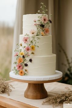 a three tiered cake with flowers on it sitting on top of a wooden table