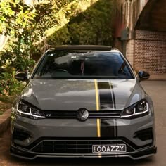 a grey car with yellow stripes parked in front of a brick wall on the side of a road