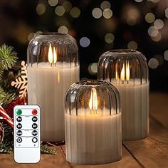 three lit candles sitting next to each other on a wooden table with christmas decorations in the background