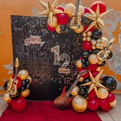 the balloon arch is decorated with gold and red balloons, black and white balls, and guitar