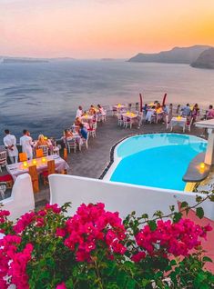 an outdoor dining area overlooking the ocean with flowers in bloom and people sitting at tables