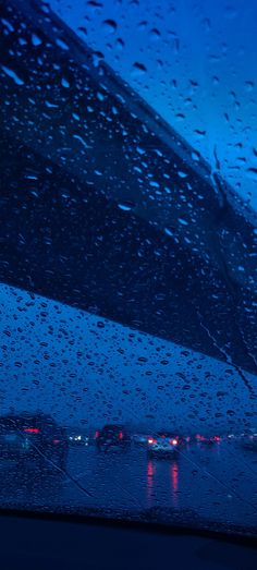 rain drops on the windshield of a car as it drives down a street at night