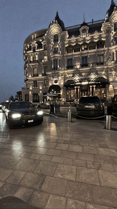 two black cars parked in front of a large building at night with the lights on