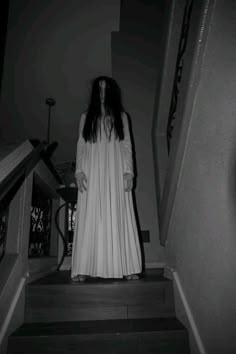 a woman in a long white dress is walking down the stairs with her hands on her hips