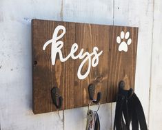 a wooden sign with two keys hanging from it's hooks on a white wall