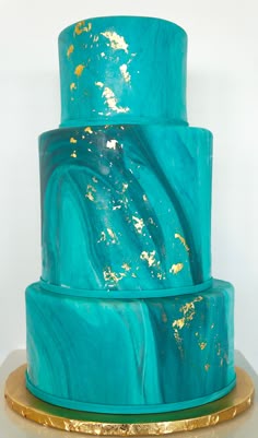 a three tiered cake with blue and gold marbled icing on a stand