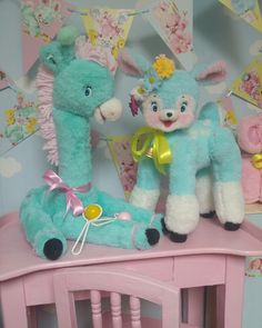 two stuffed animals sitting on top of a pink wooden table in front of a wall