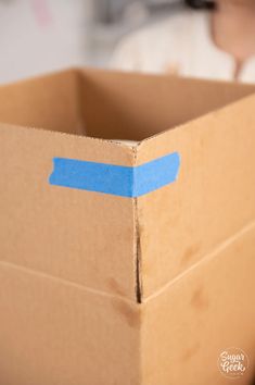 an open cardboard box with a blue tape on it and a person in the background