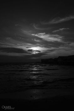 black and white photograph of the sun setting over the ocean with clouds in the sky