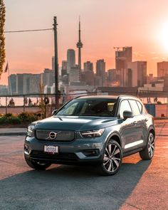 a grey volvo car parked in front of a cityscape with the sun setting