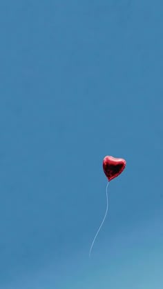 a red heart shaped kite flying in the sky with a string attached to it's tail