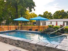 an empty swimming pool with blue umbrellas in the back ground and landscaping around it