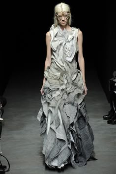a woman walking down a runway wearing a dress made out of newspaper strips and ruffles