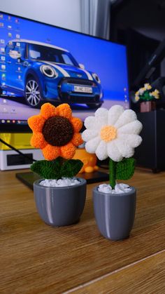two flower vases with fake flowers in front of a flat screen tv on a wooden table