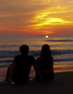 two people sitting on the beach watching the sunset
