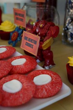 some red cookies are on a white plate and there is an iron man figure in the background