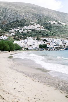 an empty beach next to the ocean with white buildings in the backgrouds