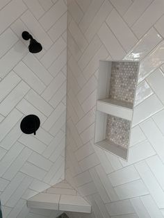 a white tiled shower with black fixtures and shelves on the wall next to it,