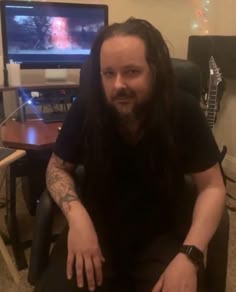 a man with long hair sitting in front of a tv