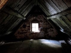 an attic with exposed brick walls and a small window in the center, surrounded by wooden beams