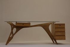a wooden desk with drawers and a glass top on it in front of a white wall
