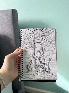 a person holding up a coloring book with an octopus and lighthouse in the ocean on it