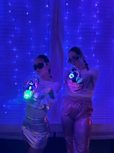 two women dressed in shiny clothing holding glowing objects
