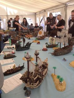 a group of people standing around a table with model ships on it