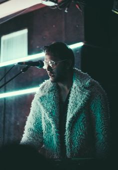 a man in a fur coat standing next to a microphone and looking into the distance