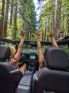 two women sitting in the back seat of a car with their hands up to the sky