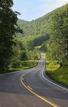 an empty road surrounded by trees and hills
