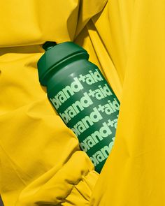 a person in yellow is holding a green water bottle with the word brand on it