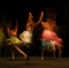 blurry photograph of people dancing in front of a black background with one person on the floor
