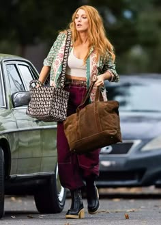 a woman with long red hair carrying a brown bag while walking down the street in front of a green car