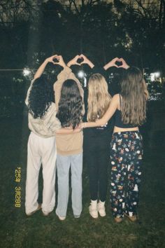 four girls are standing in the grass making a heart shape with their hands while holding each other's hands