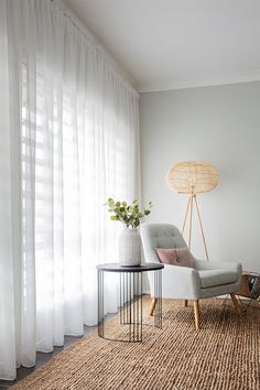 a chair and table in front of a window with sheer curtains