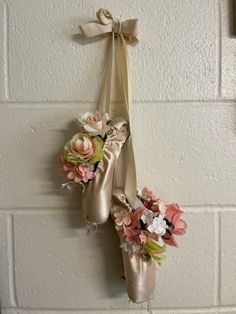 two pairs of ballet shoes hanging on a wall with flowers and ribbons attached to them
