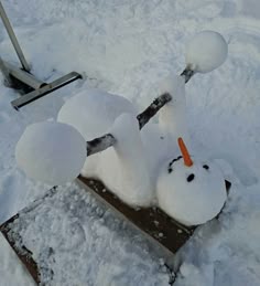 a snowman sitting on top of a piece of wood in the middle of some snow