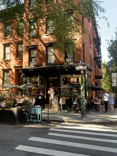 people are sitting at tables in front of an outdoor cafe on the corner of a city street