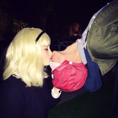 a woman with blonde hair kissing a man's face in the grass at night