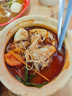 a bowl of soup with noodles, meats and vegetables in it on a wooden table