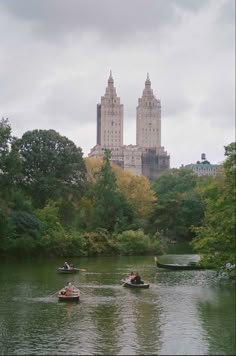 three people in small boats on a river with tall buildings in the backgroud