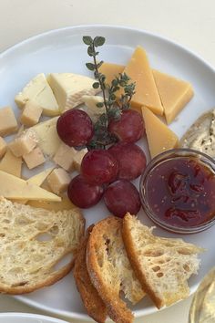 a white plate topped with bread, cheese and grapes