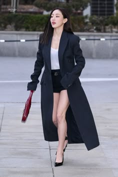 a woman walking down the street wearing a long black coat and high heeled shoes