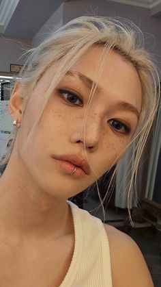 a woman with blonde hair and blue eyes wearing a white tank top looking at the camera