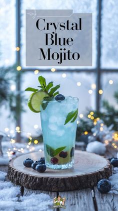 a glass with blueberries, lime and mint sitting on top of a wooden table